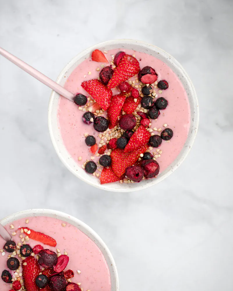 Çilek ve yaban mersiniyle süslenmiş pembe smoothie kasesi